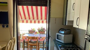A kitchen with a gas stove, microwave, and cabinets. There is a dining table with chairs and a striped awning outside. - Apartment Direct to the Beach of Scala Dei Turchi (Realmonte)