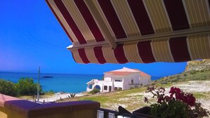 A coastal view with a building featuring a red-tiled roof and a white facade, under a striped awning. - Apartment Direct to the Beach of Scala Dei Turchi (Realmonte)