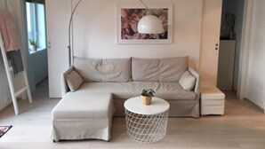 A living room with a sofa, ottoman, and a round coffee table with a plant. - StayPlus Ocean View Apartment Balcony (Kristiansand)