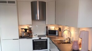 A modern kitchen with white cabinets, a stainless steel range hood, a microwave, and a sink. - StayPlus Ocean View Apartment Balcony (Kristiansand)