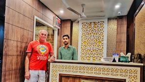 A reception area with a wooden reception desk, a ceiling fan, and a decorative wall panel. - Hotel Janki Inn Varanasi (Varanasi)