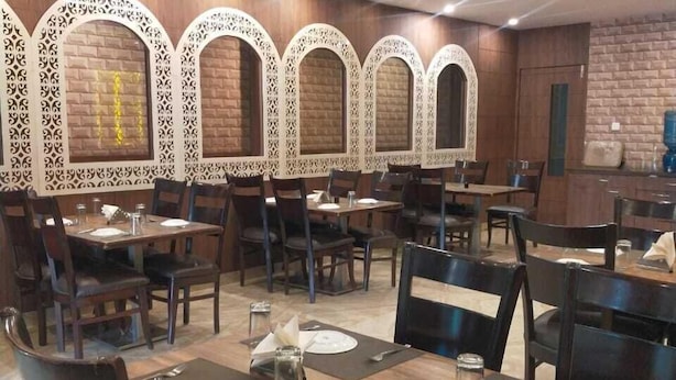 A restaurant with multiple tables and chairs, decorative wall panels, and a brick wall. - Hotel Janki Inn Varanasi (Varanasi)