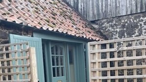 Ein hölzernes Tor führt zu einem Haus mit einer grünen Tür und einem Ziegeldach.