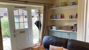 Ein Wohnzimmer mit einem dunkelbraunen Ledersofa, gemusterten Kissen, einem Bücherregal und einem großen Fenster mit Vorhängen.