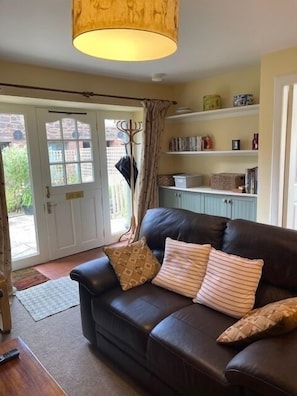 Relax in this inviting living room with a comfortable sofa, a warm-toned lamp, and a door leading to an outdoor area.