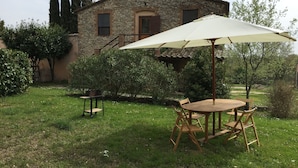 A stone house with a garden patio featuring a wooden table and chairs, an umbrella, and a small table with a chair. - Silence and Relaxation in Countryside of Umbria (Amelia)