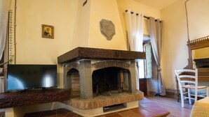A room with a stone fireplace, a television on a stand, a white chair, and a bed with a quilt.