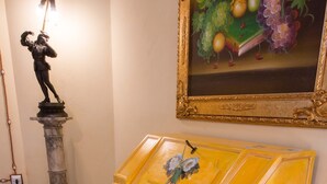 A statue on a pedestal, a framed painting, and a yellow cabinet with floral designs.