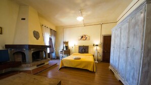 A room with a fireplace, a bed with a yellow bedspread, wooden flooring, and a large wardrobe.