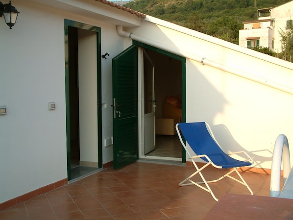 A balcony with a blue chair, a white wall, and a green door.