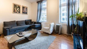 A modern living room with a grey sofa, a white armchair, a glass coffee table, and a potted plant. - StayPlus Comfy 1BR Apt - Hip Area (Oslo)
