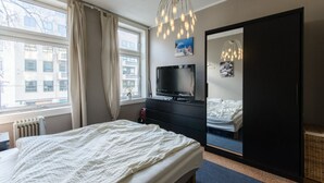 A hotel room with a large bed, a TV, a wardrobe, and a window with curtains. - StayPlus Comfy 1BR Apt - Hip Area (Oslo)