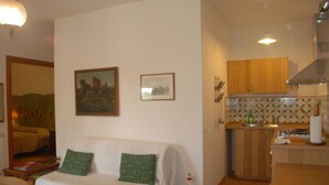 Una sala de estar con sofá, una mesa de comedor y un área de cocina con armarios de madera y salpicadero de azulejos.