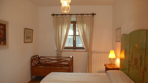 Un dormitorio con una cama de madera, una ventana con cortinas, un radiador y una lámpara sobre una mesita de noche.