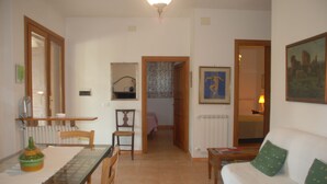 Una sala de estar con sofá, una mesa de comedor con sillas, una zona de cocina y un pasillo que lleva a un dormitorio.