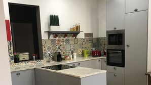 Una cocina moderna con una isla central, horno empotrado y microondas. Se observan armarios, un lavamanos y una encimera con diversos objetos.