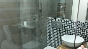 Un baño moderno con ducha envuelta en vidrio, inodoro blanco y tocador de madera con lavamanos.
