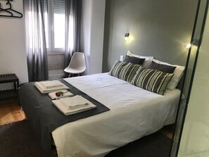 Uma cama bem arrumada com almofadas e toalhas dobradas, uma cadeira e uma janela com cortinas.
