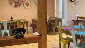 Un comedor con mesas y sillas de madera, varios relojes en la pared y lámparas colgantes.
