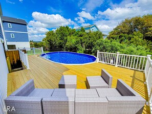 A backyard with a swimming pool, wooden deck, and wicker furniture.