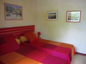 A bed with red and orange bedding, a nightstand with a lamp, and three framed pictures on the wall. - Le Chalet des Althéas for 4 people (CHAMAGNIEU)