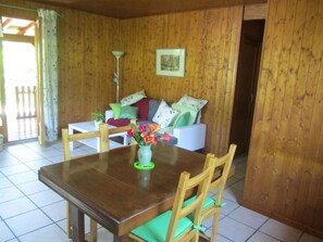 A wooden-paneled room with a dining table, chairs, a sofa, and a small table with a vase of flowers. - Le Chalet des Althéas for 4 people (CHAMAGNIEU)