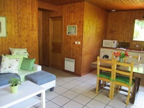 A cozy room with a sofa, a dining table with chairs, a microwave, and a washing machine. - Le Chalet des Althéas for 4 people (CHAMAGNIEU)