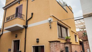 A two-story building with a balcony, a door, and a small brick structure with potted plants. - Euthymus Apartment Calabria- Jasmine Coast (Locri)