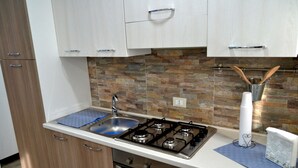 A modern kitchen with a gas stove, sink, and wooden cabinets. - Tukory - Flat For Rent - City Center Palermo (Palermo)