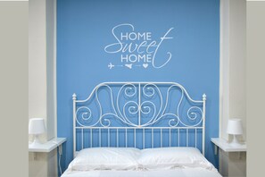 A bedroom with a blue wall, a white metal headboard, and a sign that says "HOME Sweet HOME". - Tukory - Flat For Rent - City Center Palermo (Palermo)