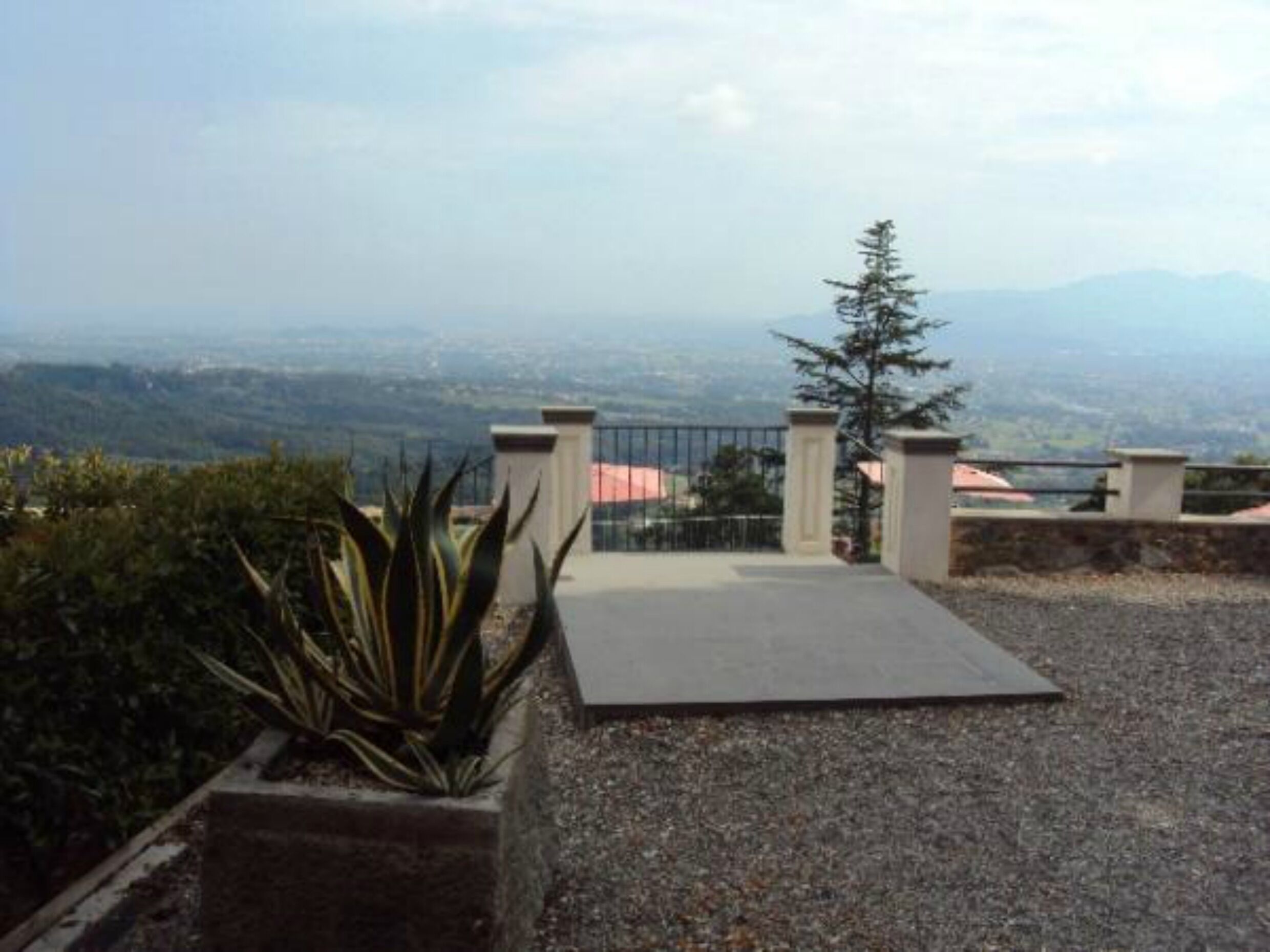 Una terraza en la azotea con vistas a montañas distantes, un portón metálico y una planta en maceta.