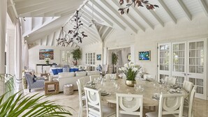 Une salle à manger spacieuse avec un plafond haut et des meubles blancs, comprenant une table centrale mise pour le repas.