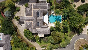 Vue aérienne d’une maison dotée d’une piscine, entourée d’une végétation luxuriante et de palmiers.