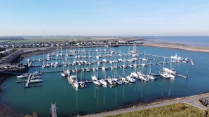 Marina com vários barcos atracados, rodeada por campos abertos e turbinas eólicas ao longe.