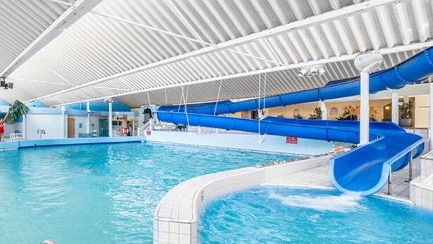 Piscina interna com escorregador azul e plataforma de mergulho.
