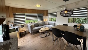 Uma cozinha moderna com micro-ondas, fogão e armários de madeira. Há um sofá cinza com almofadas, uma mesa de madeira redonda e cadeiras pretas.