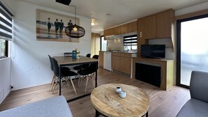 Cozinha compacta com armários de madeira, área de refeições com mesa e cadeiras, uma televisão e um quadro na parede.