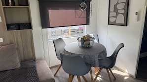 Uma área de refeições com mesa redonda, cadeiras cinzas, um cesto e um lustre.
