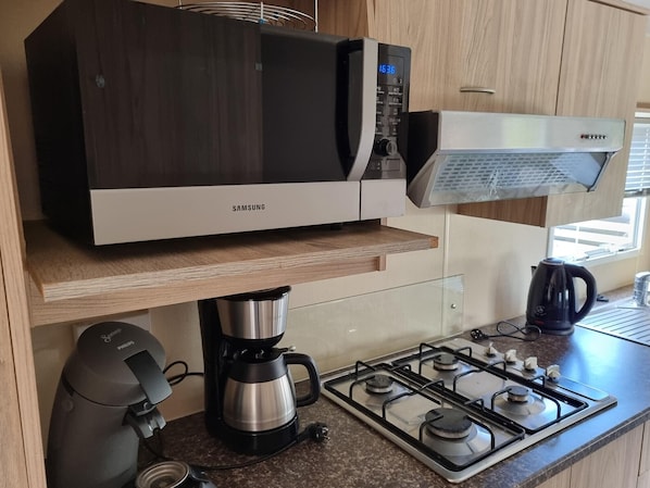 Een moderne keuken met een ingebouwde magnetron, koffiezetapparaat en gasfornuis.