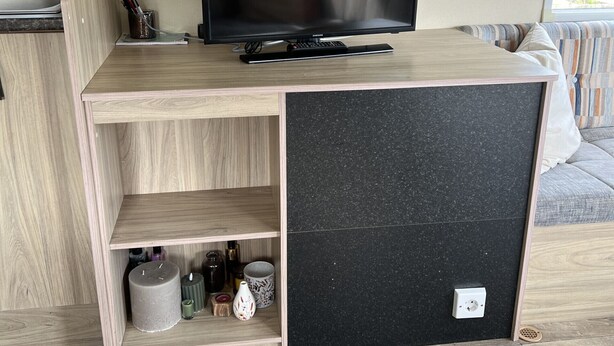 A modern living room with a flat-screen TV on a wooden console table, a small shelf with decorative items, and a power outlet on the console. - RBR 166 - Beach Resort Kamperland (Kamperland)