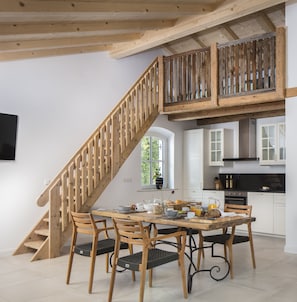 A dining area with a wooden staircase leading to a loft. There is a kitchen with white cabinets and a black countertop. - Ferienwohnung Chiemsee (Breitbrunn a. Chiemsee)