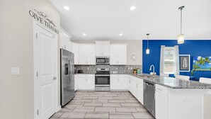 A modern kitchen with white cabinets, stainless steel appliances, and a blue accent wall.