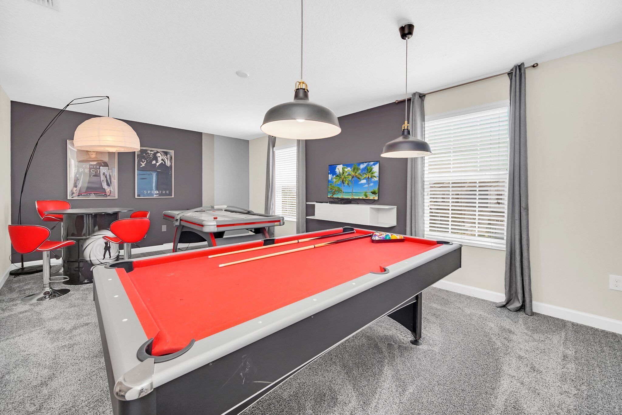 A pool table with red felt, a billiards cue, and a pool table with a red felt. There are two red chairs and a table with a billiard cue rack.