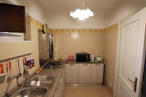 Cocina compacta con estufa a gas, pileta y microondas. Hay placares, un reloj y un estante con objetos.