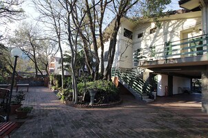 A courtyard with a brick floor, potted plants, a bench, and a staircase leading to a building with a balcony.