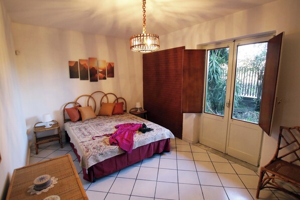 Quarto com cama, guarda-roupa de madeira, janela com vista para o verde e luminária suspensa.
