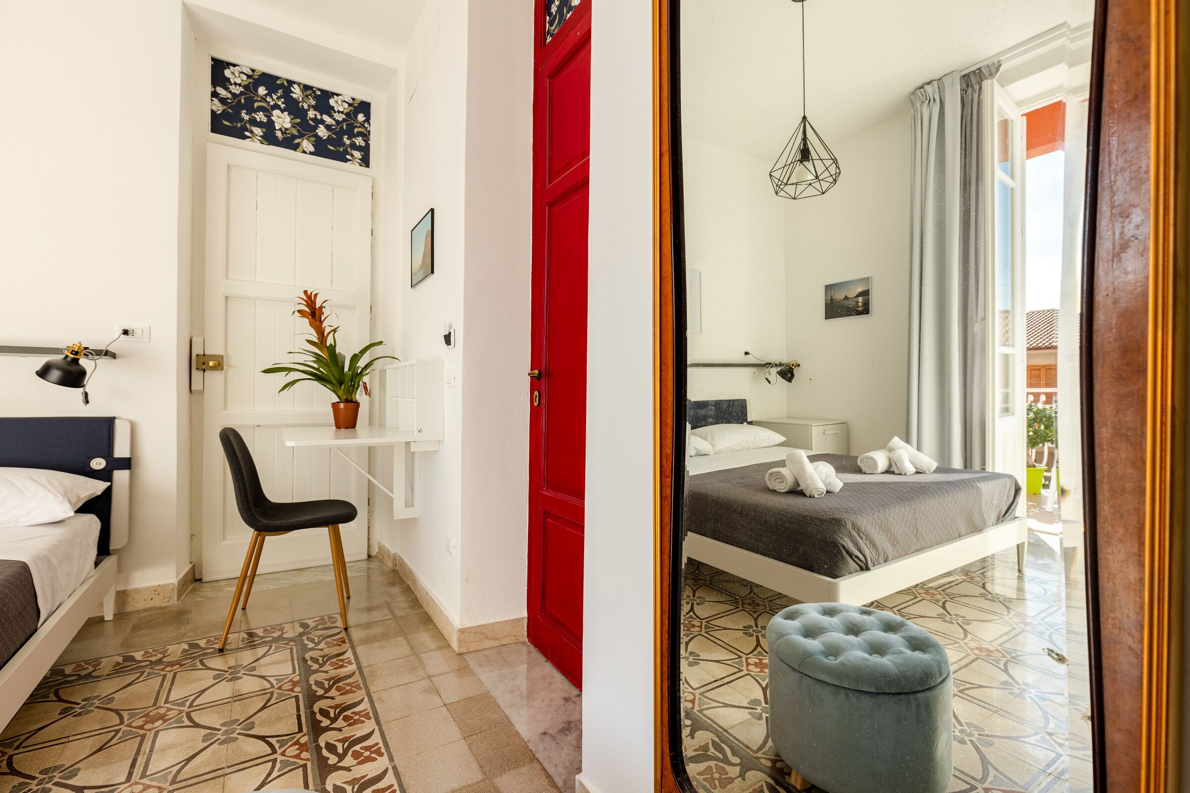 A bedroom with a bed, a desk, a chair, and a red door.