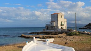A coastal building with a white facade and red-tiled roof, situated near the sea with boats docked nearby. - Villa Edera Rental Rooms (Santa Flavia)