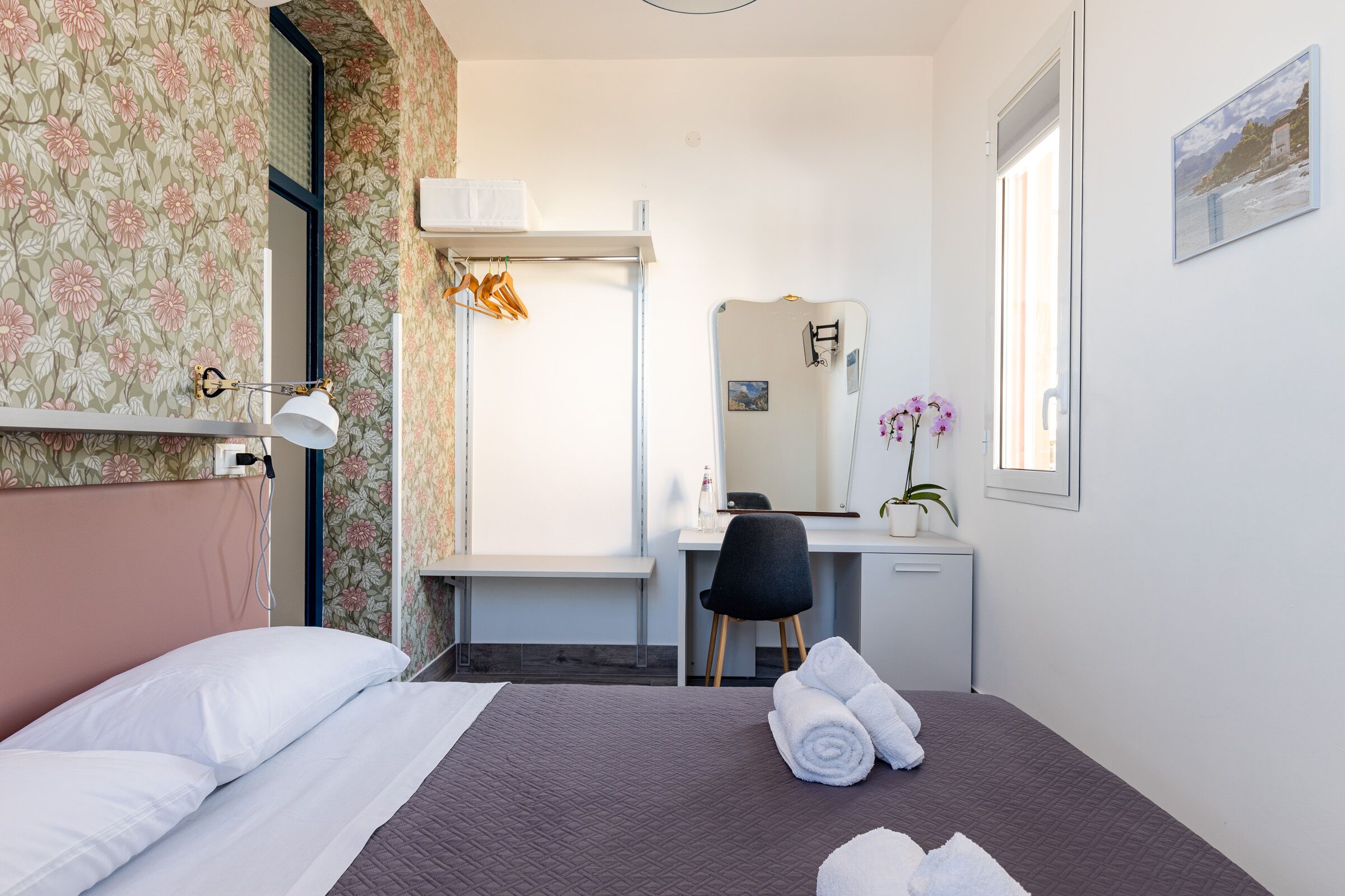 A hotel room with a bed, a desk, a chair, a mirror, and a window with a view.