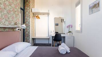 A hotel room with a bed, a desk, a chair, a mirror, and a window with a view.